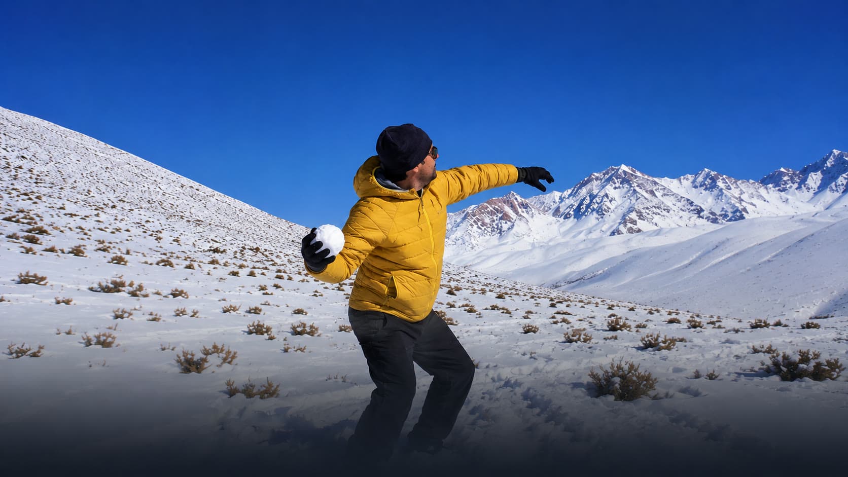 Persona jugando con nieve frente a la cordillera nevada en un día de invierno en San Juan